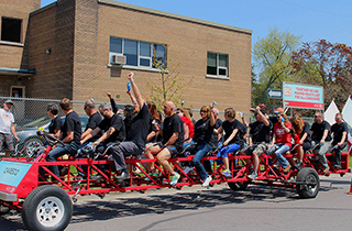 20 plus Cameco employees riding a large red bike outside on a sunny day